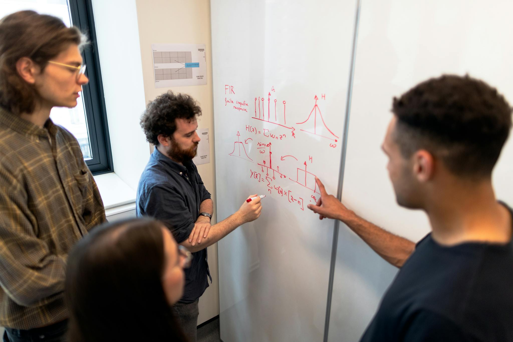 Group of engineers discussing data on a whiteboard during a team meeting.